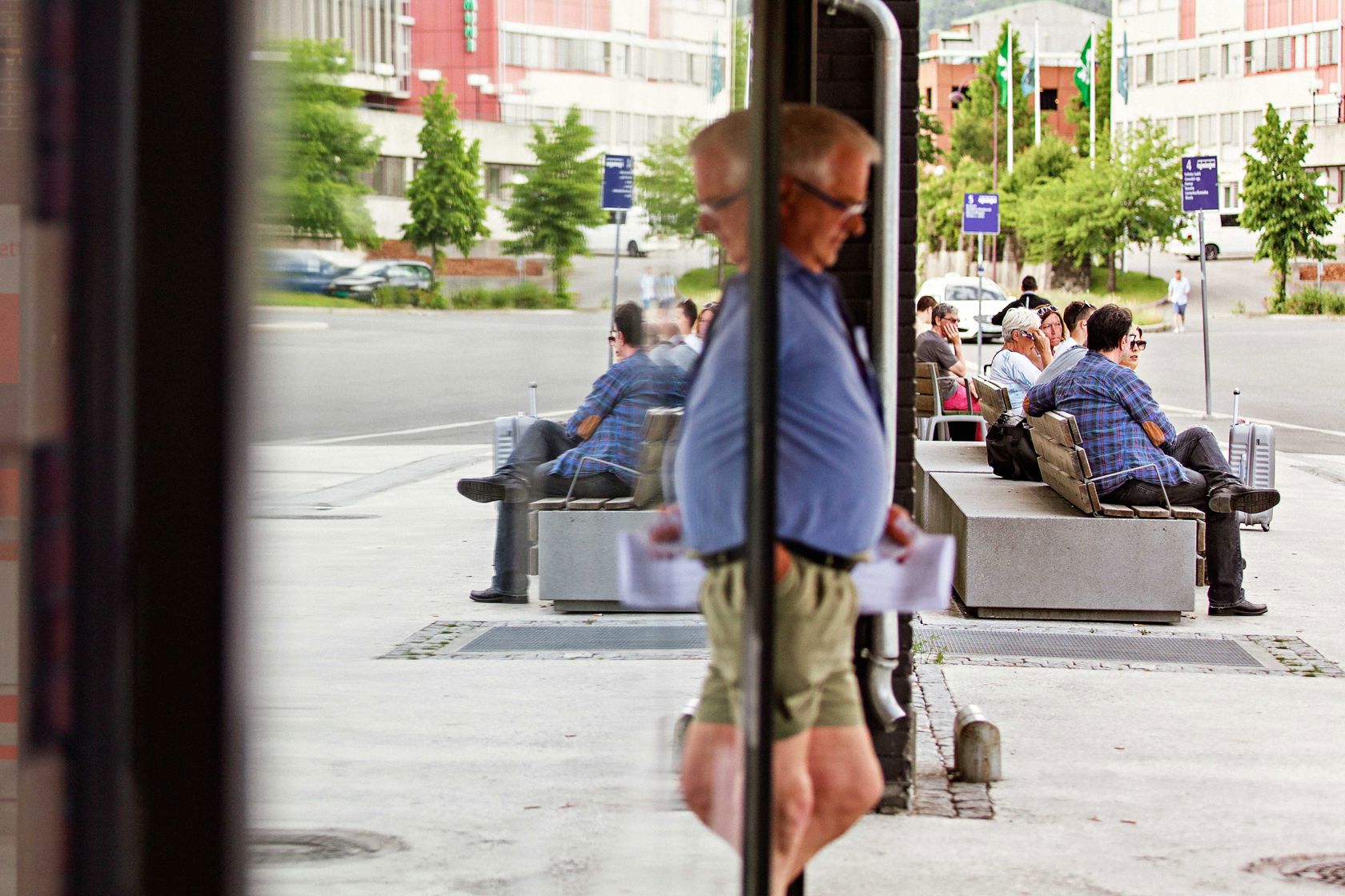 Mennesker som venter på transport ved Lillehammer kollektivknutepunkt. Gjenspeil i vindu.