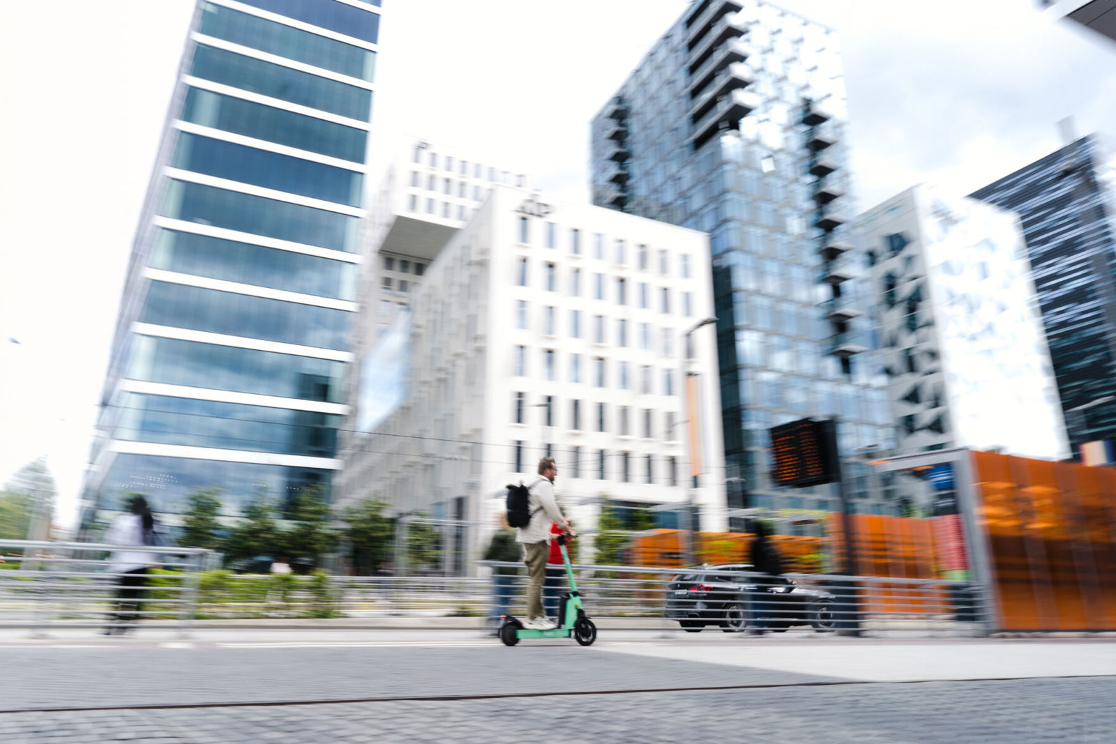 Høye bygninger og en stasjon for kollektivtrafikk. Menneske på sparkesykkel.