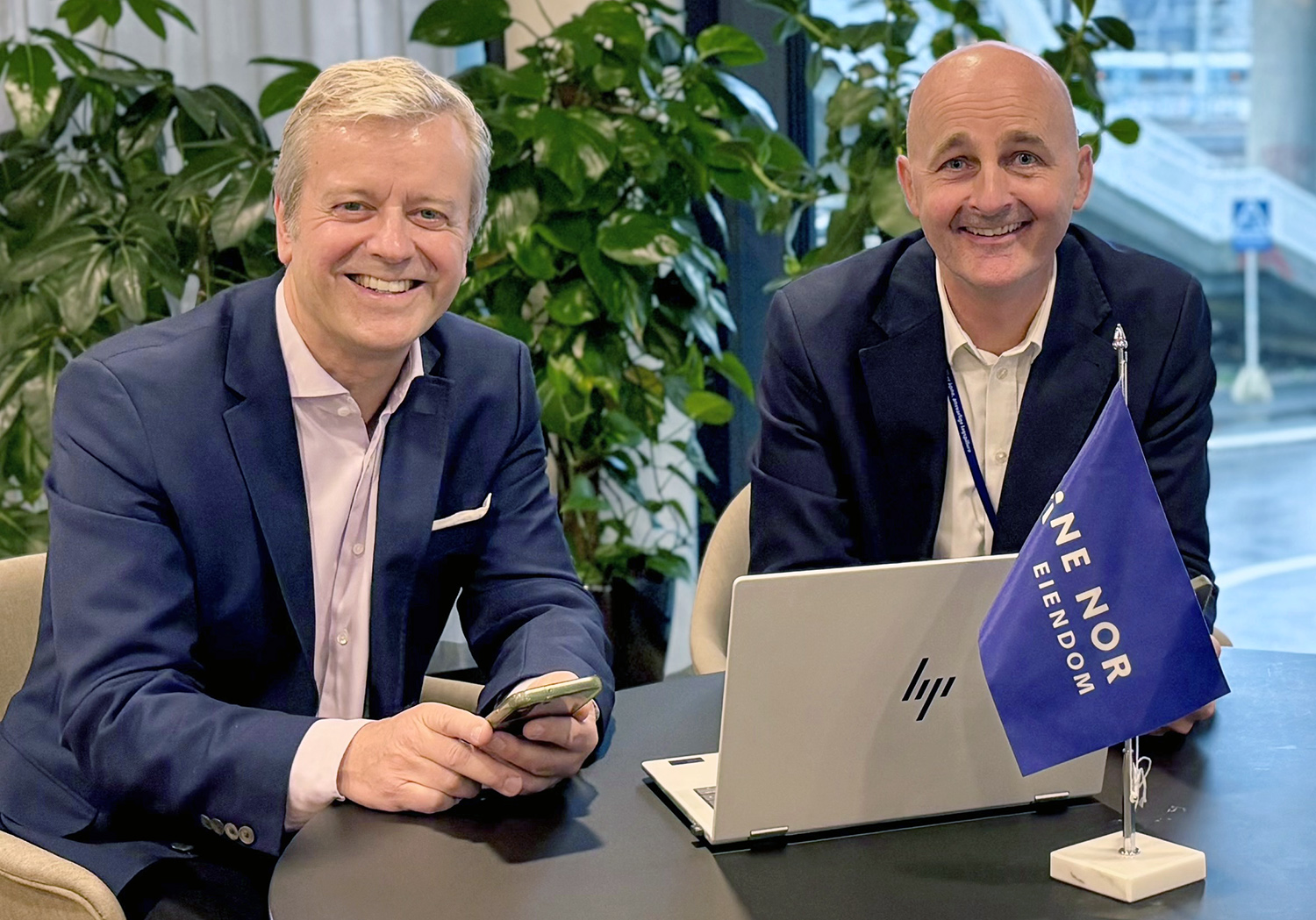 Personene sitter smilende ved et bord med en PC og et Bane NOR-flagg.