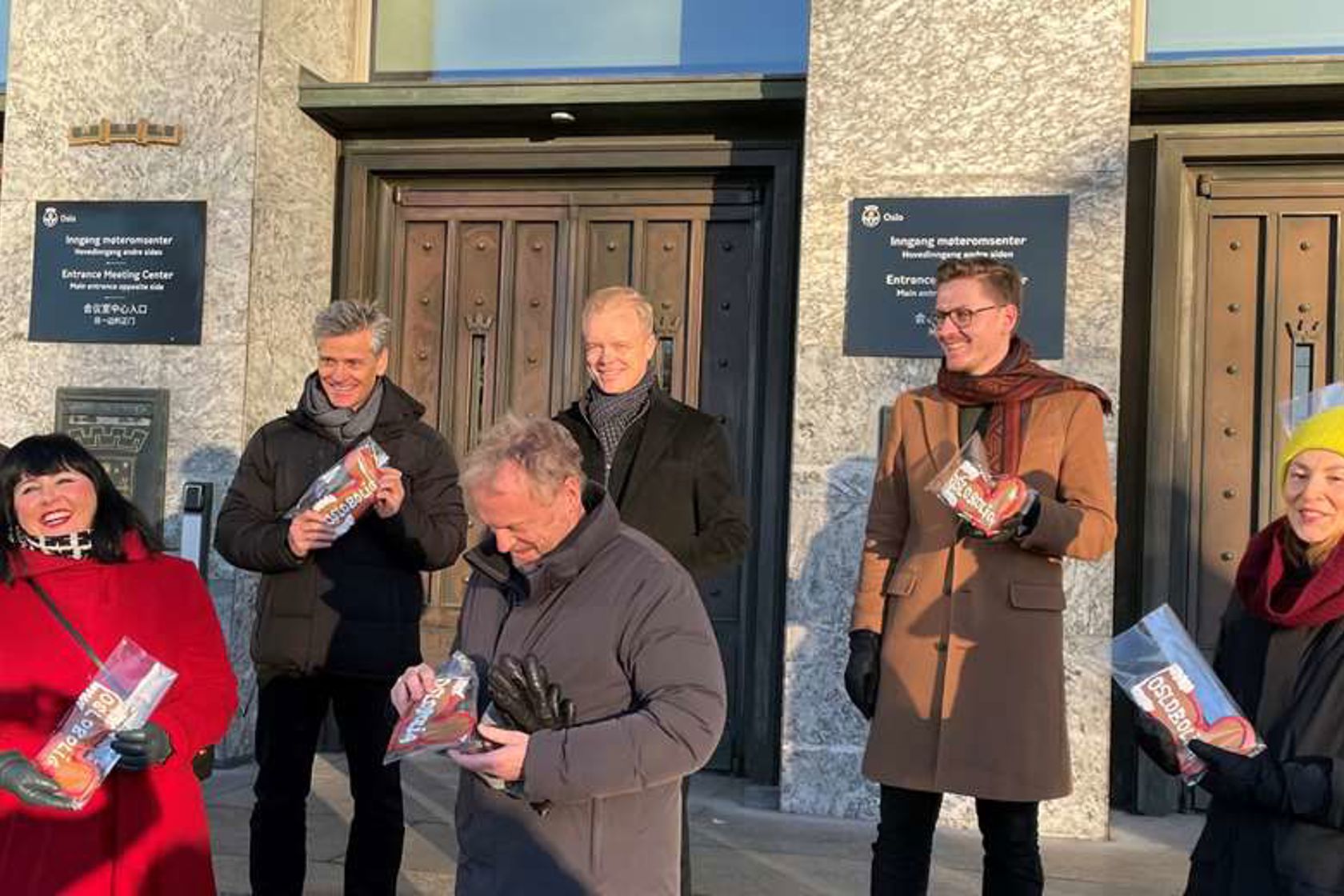 Åtte mennesker smiler på Rådhustrappa i Oslo. Dette er eierne av Oslobolig.