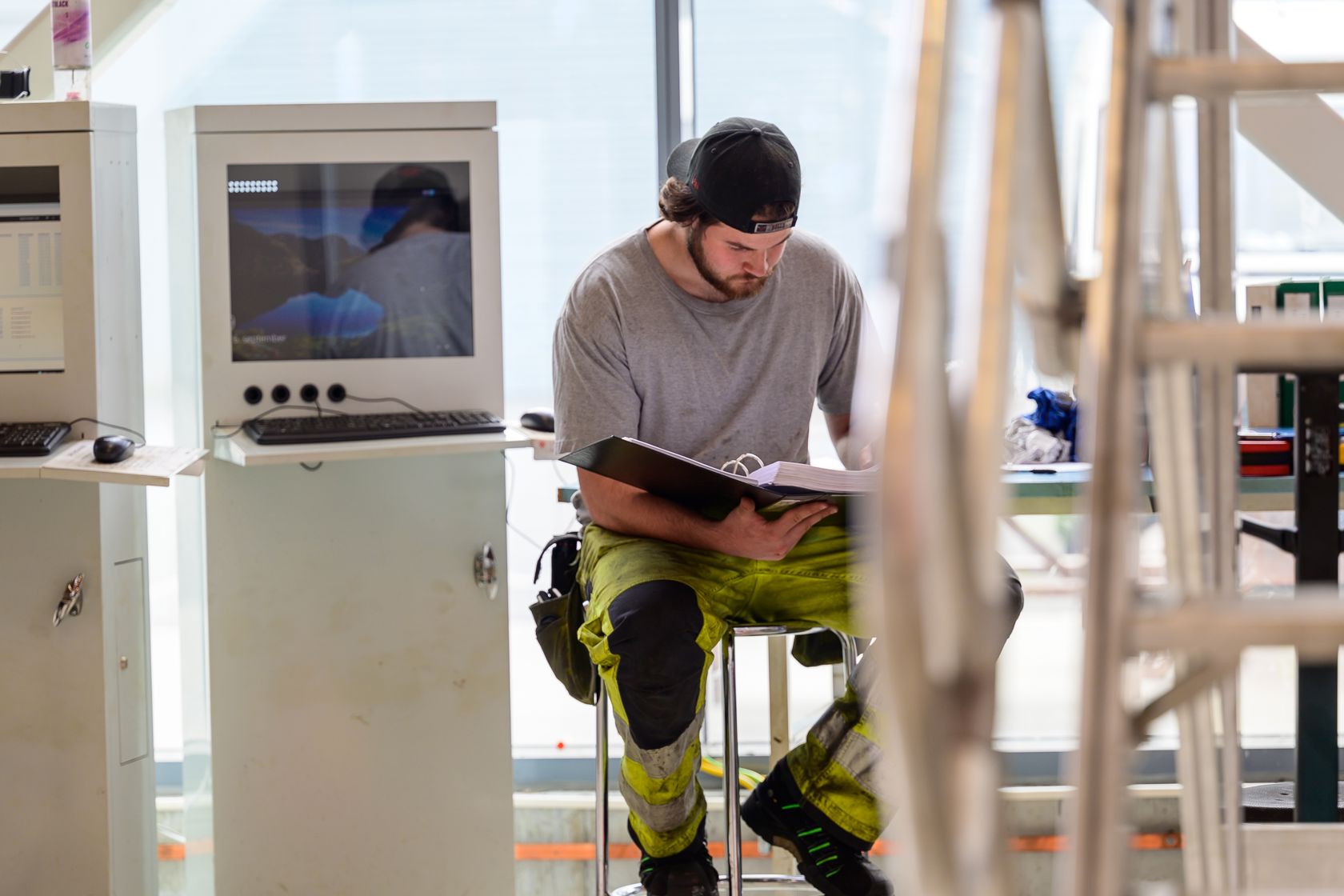 En driftsteknikker ikledd arbeidstøy som sitter å jobber. Skjermer og utstyr i rommet.