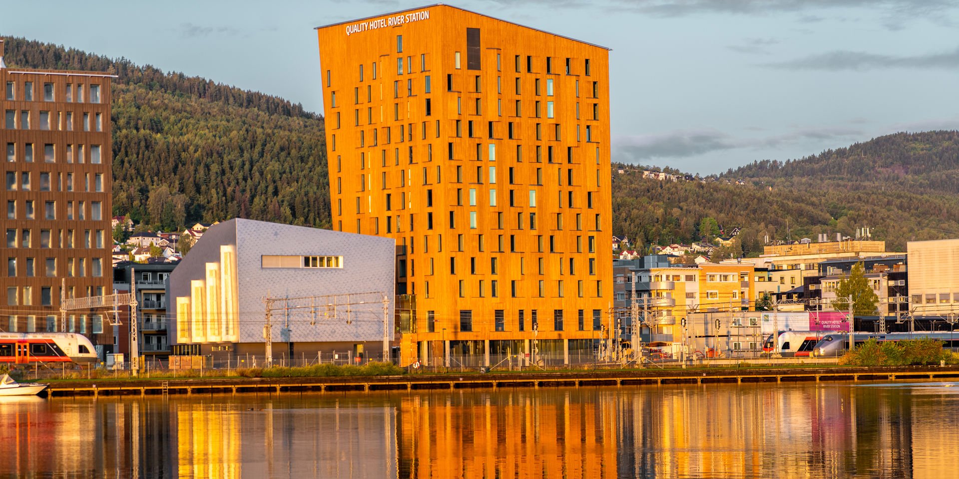 næringsbygg og hotell rett ved en togstasjon. Byggene er i ulike høyder med en elv foran.