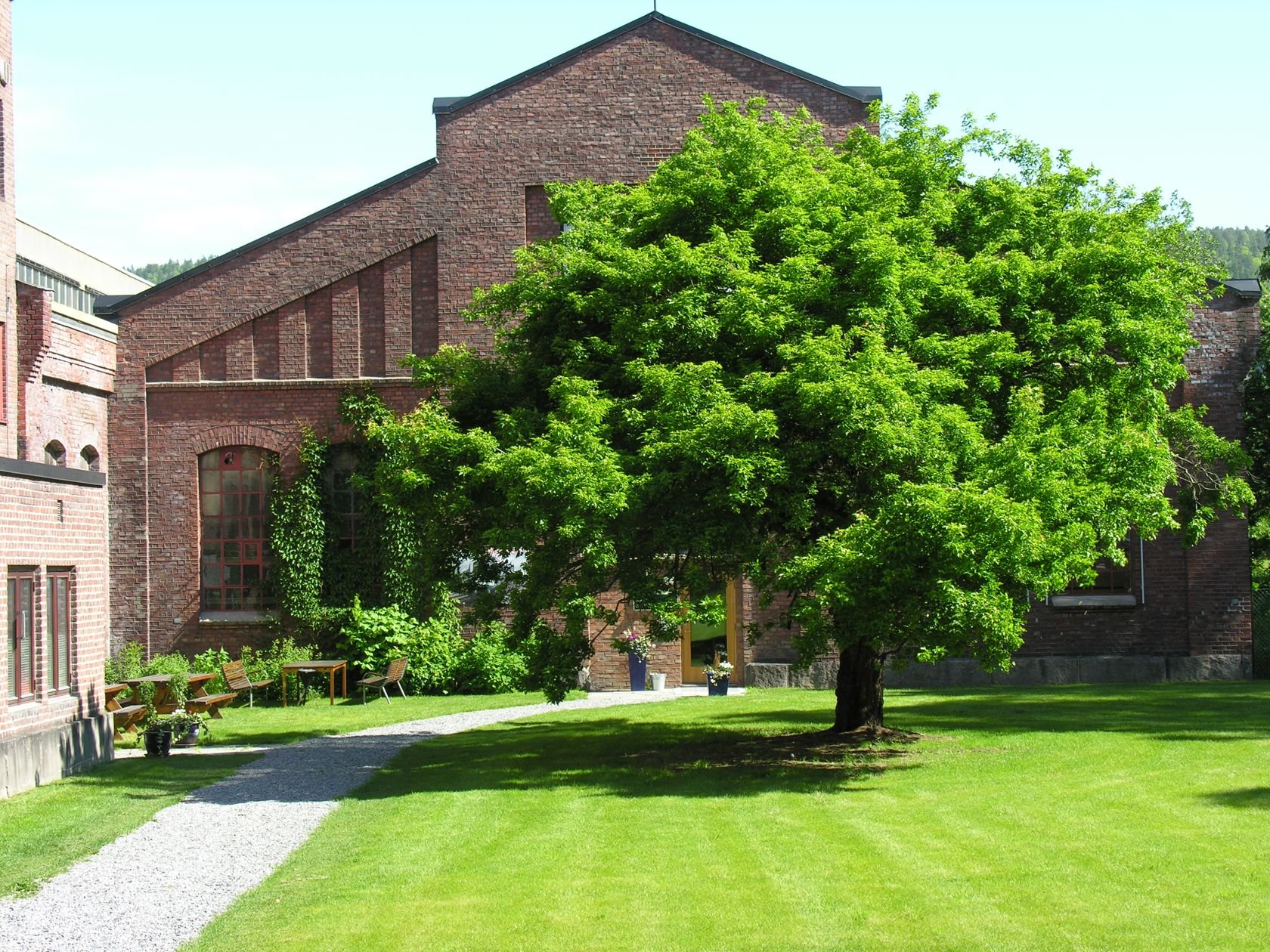 to gamle mursteinsbygg med stor tre og grønn plen foran